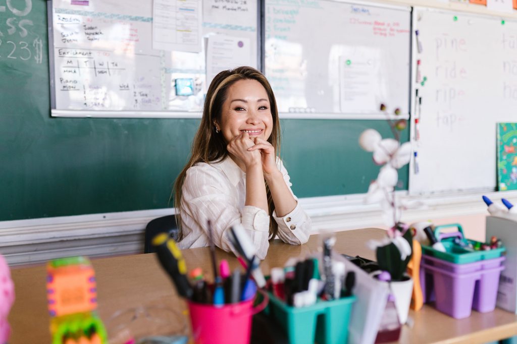 teacher sitting in front of whiteboards and chalkboards